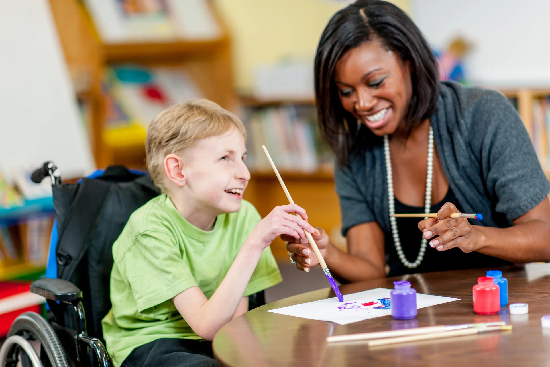 Special education advocate painting alongside a smiling boy who uses a wheelchair