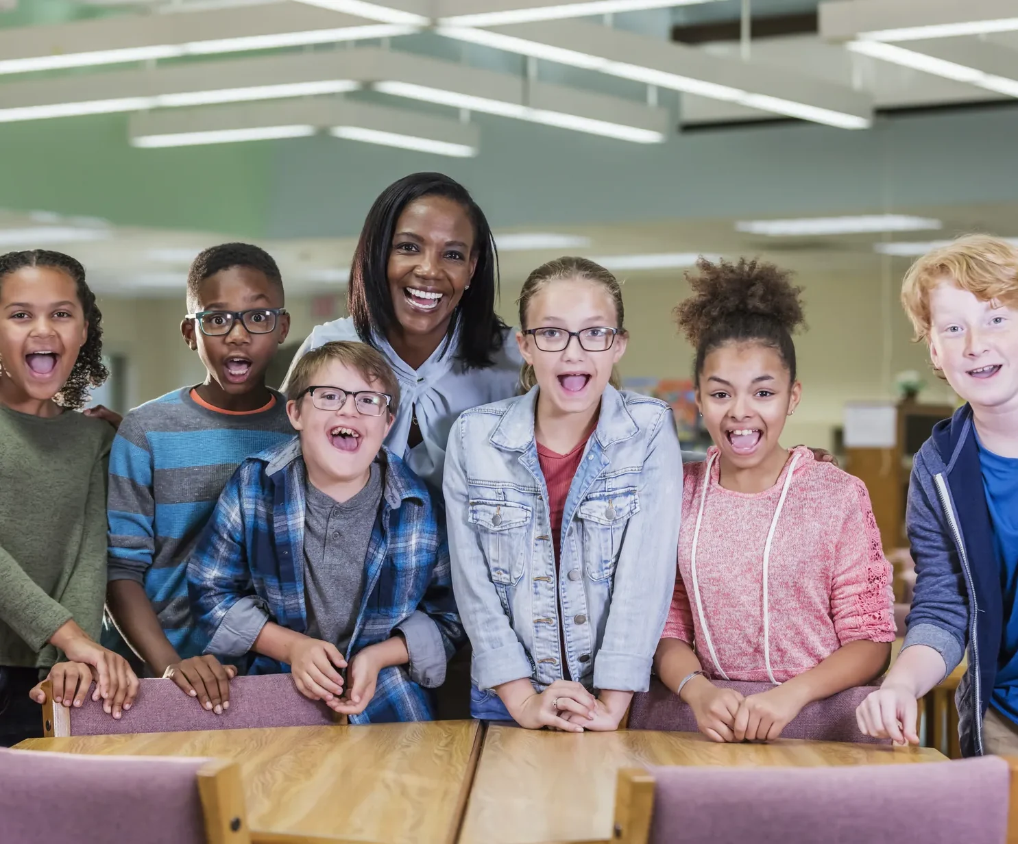 Smiling teacher with a diverse group of middle-school students in a school library