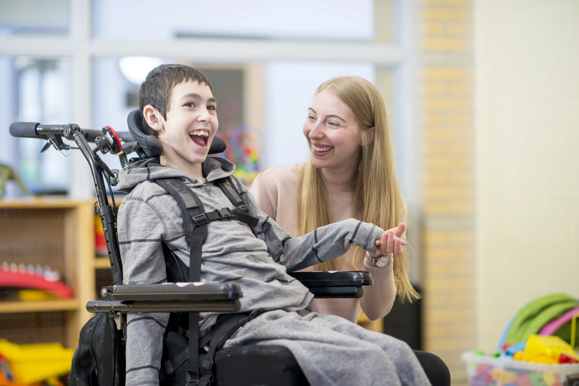 Teenage student with a disability laughing with a caregiver in a classroom